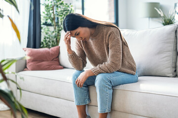 Worried woman thinking about problems sitting on couch in the living room at home
