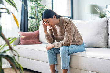 Worried woman thinking about problems sitting on couch in the living room at home