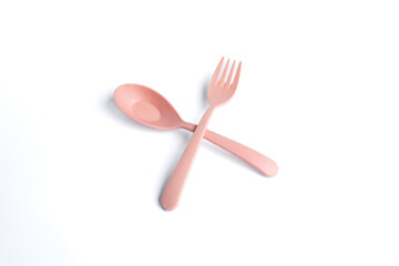 Stylish pink spoon and fork crossed on a white background, showcasing modern and minimalist tableware design