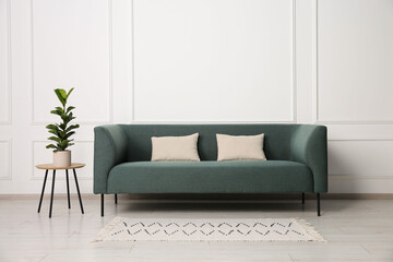 Stylish sofa, pillows and side table with houseplant near white wall indoors