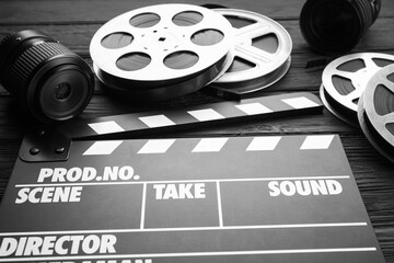 Movie clapper, camera lens and film reels on black wooden table, closeup