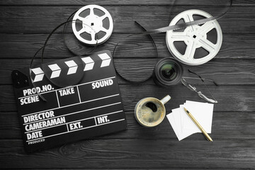 Movie clapper, film reels and camera lens on black wooden table, flat lay