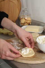 Woman making pirozhki (stuffed pastry pies) with cottage cheese at countertop indoors, closeup