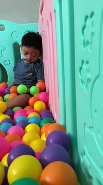 A child living with cerebral palsy is playing in a colorful ball pool in the occupational therapy room. A young child with a nasogastric tube sits among a colorful sea of plastic balls. 