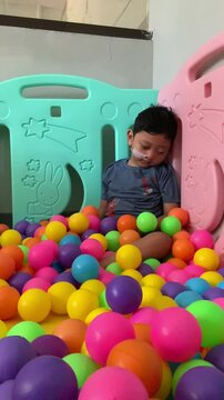 A child living with cerebral palsy is playing in a colorful ball pool in the occupational therapy room. A young child with a nasogastric tube sits among a colorful sea of plastic balls. 