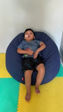 Children who use NGT (nasogastric tube) or a probe on their nose are sleepy while sitting on a blue bean-shaped sofa