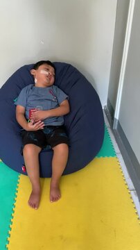 Children who use NGT (nasogastric tube) or a probe on their nose are sleepy while sitting on a blue bean-shaped sofa