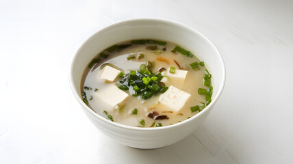 A photo of a white bowl containing miso soup with a few tofu cubes and green onions floating on the 
