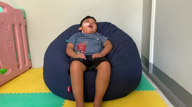 Children who use NGT (nasogastric tube) or sonde on their nose are yawning while sitting on a blue bean-shaped sofa