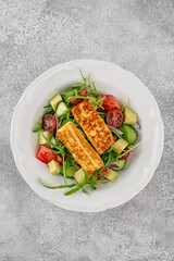 Salad with grilled halloumi cheese, tomatoes, avocado, cucumber and olive oil on a concrete background. Healthy food. Top view