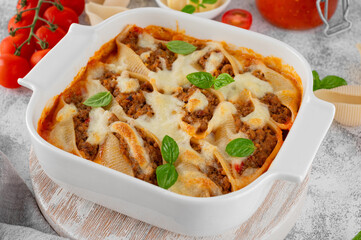 Baked stuffed pasta conchiglioni shells with meat, tomato sauce, cheese and basil in a white ceramic form. Italian cuisine.
