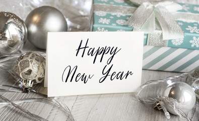 A sign that reads Happy New Year stands on the table with gift boxes in the background. Christmas background with decorations from balls and garlands. Christmas or festive concept.