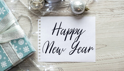 Notepad on the table with the text HAPPY NEW YEAR. Christmas background with decorations from balls and garlands. Delicate shades. Christmas or festive concept.