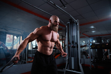 Bald Caucasian bodybuilder training chest using cable crossover in gym. 