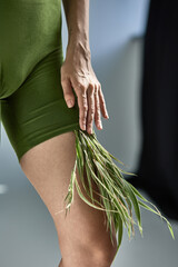 Person in green outfit with grass details touching leg gracefully, nature and fashion fusion concept