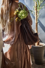 Elegant woman with floral bouquet, draped in brown, sunlight streaming in, elegant fashion...