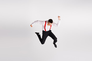 Energetic young man in elegant attire showing dynamic dance move on a white background