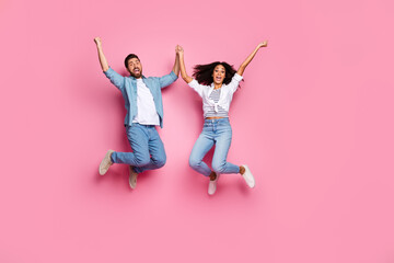 Cheerful young couple in casual outfits jumping in excitement on a pink background