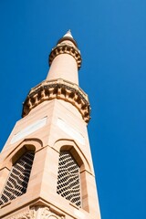 A tall minaret against a clear blue sky, showcasing intricate architectural details.