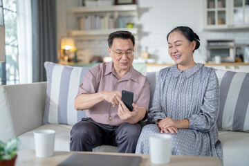 An elderly couple sits together in their cozy living room, smiling and enjoying a moment as they look at something on a smartphone. Their warmth and affection capture a peaceful home atmosphere.
