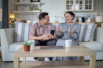 An elderly couple sits together in their cozy living room, smiling and enjoying a moment as they look at something on a smartphone. Their warmth and affection capture a peaceful home atmosphere.