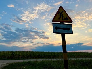 Road sign indicating road repair against a sunset sky and cornfield background. Captures a rural scene with vibrant evening colors and the contrast of infrastructure and agriculture