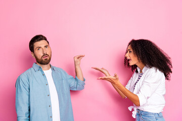 Young couple arguing with expressive gestures against a vibrant pink backdrop in casual wear