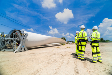 Engineers in high visibility gear assess a large wind turbine blade at a construction site under a...