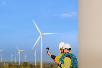 Two engineers wearing high visibility safety jackets and helmets measure wind speed with an...