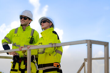 A team of engineers in high visibility safety gear stand together at a wind farm, conducting...