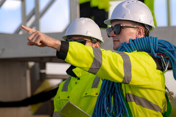 Two engineers in safety helmets and high visibility jackets engage in a field inspection. One is pointing while carrying a safety rope, highlighting communication, safety, and teamwork.