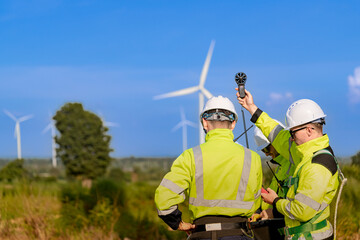 A team of engineers in high visibility safety gear stand together at a wind farm, conducting inspections and discussing renewable energy projects. Wind turbines surround them under a clear sky. © ultramansk