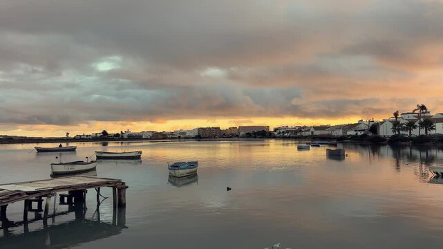 Tranquil sunrise illuminates barbate harbor in andalusia, spain, with fishing boats gently swaying on calm waters, reflecting the colorful sky and creating a serene coastal scene