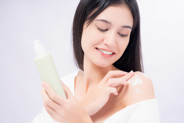 A smiling young woman gently applying moisturizing lotion to her shoulder while holding a skincare bottle, highlighting beauty and self-care against a soft white background