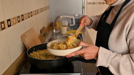 Person serving homemade vegetable paella in a kitchen setting