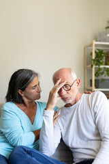 Vertical portrait of mature woman comforting sad man sitting on the couch at home living room. Copy space