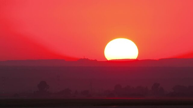Cinematic view of orange yellow and red sunset sky with clouds. End of the day. Dusk at summer. Epic sun set with large circle as sun goes down to twilight. Evening sky