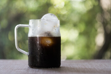 Iced americano coffee in glass with handle against nature background