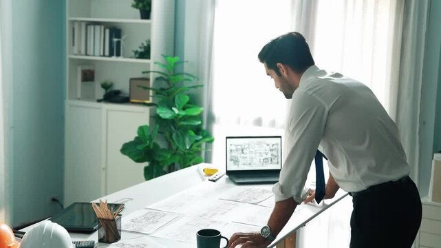 Architect engineer using laptop planning house design at office while sitting at meeting table with blueprint and equipment scatter around.Skilled civil engineer working at blueprint. Alimentation.