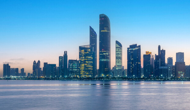 "Abu Dhabi Skyline: Night-to-Day Transition with Water Reflection from the Breakwater"