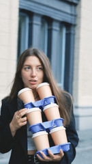 Pretty woman with long hair in office black jacket walking to work carrying many cups of takeaway...