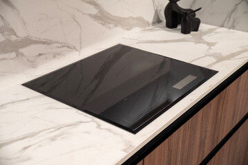 Sleek black induction cooktop integrated into a modern marble kitchen countertop