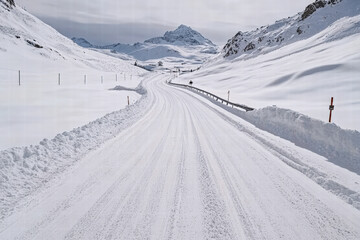 A tranquil snow-covered road twists through a majestic winter mountain scene, showcasing nature's serene beauty and the pristine wilderness.