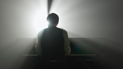 Pianist playing on the black grand piano on dark concert stage against spotlight, back shot isolated on black studio background. Artist performing in concert hall. © kinomaster