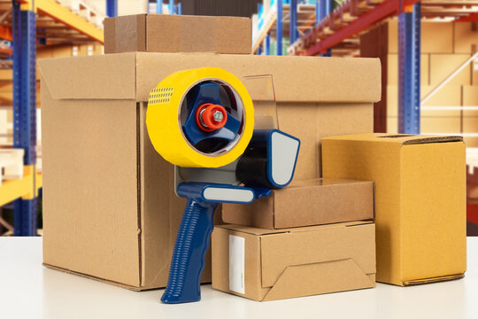 Warehouse packaging materials. Dispenser with tape near cardboard boxes. Parcels and sticky tape on table. Scotch tape for packing boxes. Packaging materials among racks with parcels