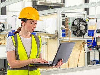 Female engineer near conditioning equipment. Technologist inside factory holds laptop. Engineer...