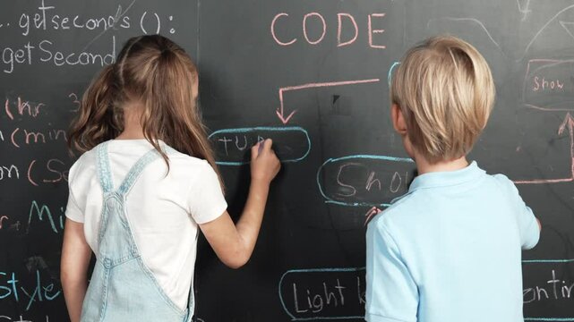 Caucasian girl writing blackboard with engineering prompt or coding, programing system written in STEM technology classroom and turnaround to looking at camera while boy showing thumb. Erudition.