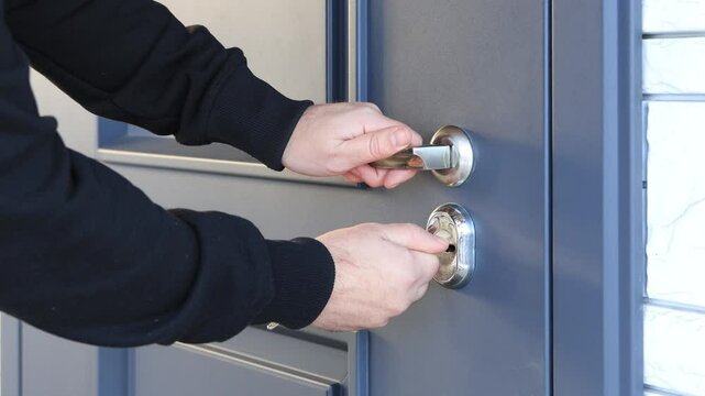 Trying to open a jammed lock on an entrance door - hands, keyhole, keys close-up. The intruder tries to open the door and cannot get inside the house.