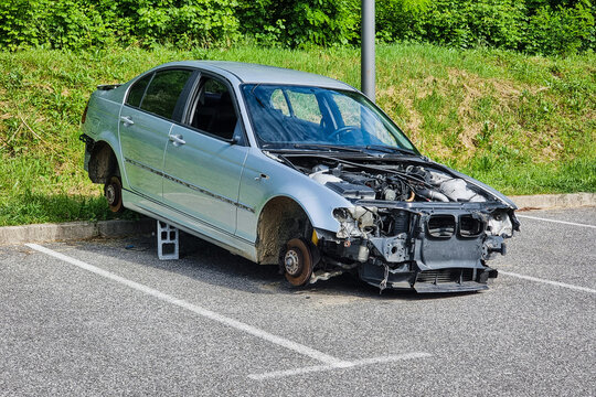 Vandalized car stands on bricks with removed wheels and front engine parts