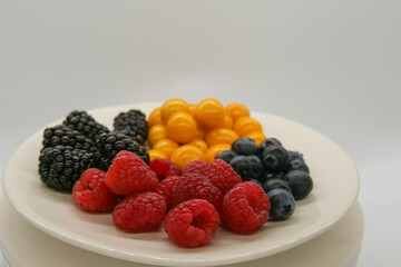 Brightly colored fresh berries on a white plate in front of a white background